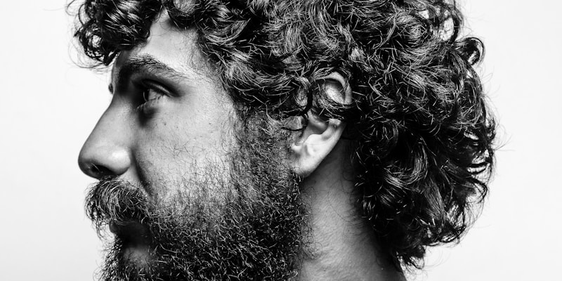 Black and white profile portrait of a man with curly hair and a beard, looking ahead in thought
