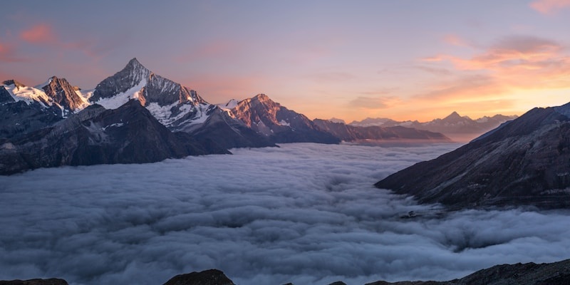 Snow-capped mountain range rising above a sea of clouds at sunrise